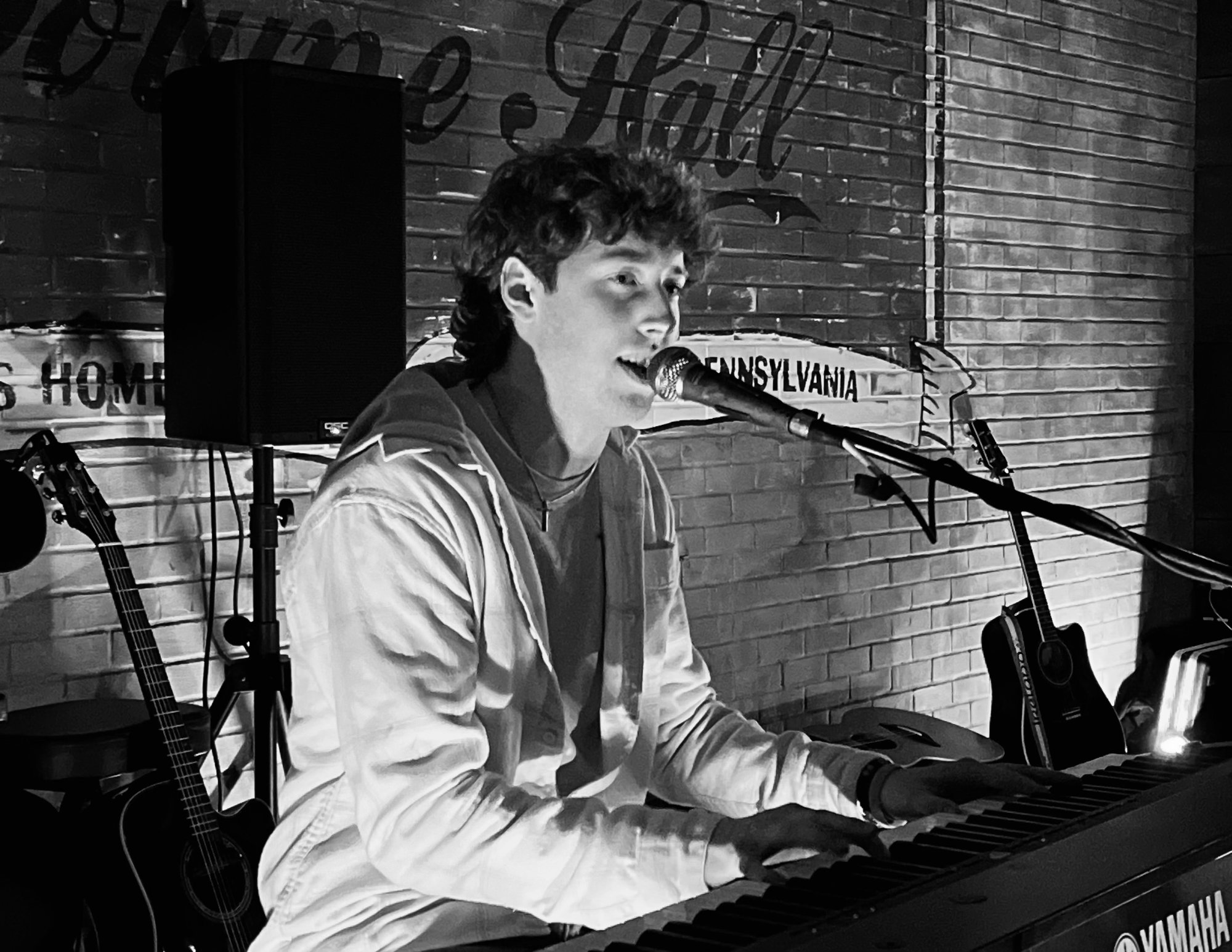 Aidan Boyce singing at the keys, guitars racked behind him